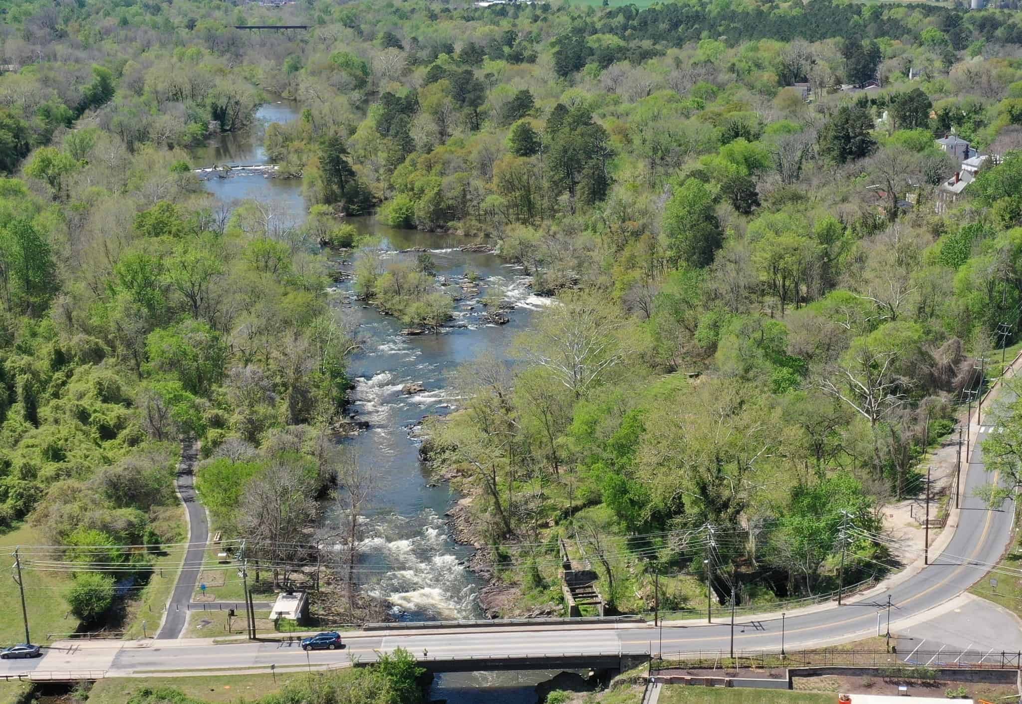 Drone shot of the falls of Appomattox River with car bridge in foreground and spring-green trees lining either side of the river.